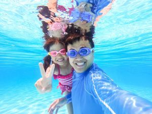A man and his daughter taking a selfie underwater in a swimming pool